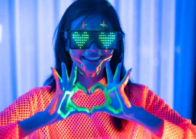 A tween with vibrant neon face paint and glasses making a heart shape with her hands at a kids' disco party